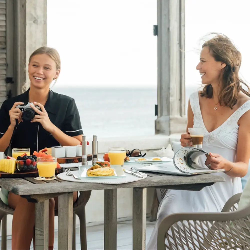 Two women laughing over breakfast by the sea