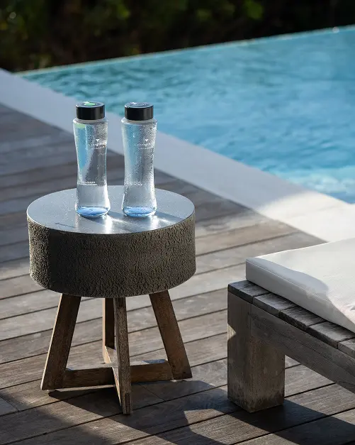 Two Ambergris Cay glass water bottles on a side table by the pool